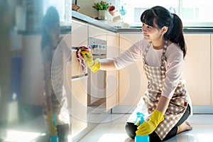 Asian woman wearing rubber protective gloves cleaning kitchen cupboards in her home during Staying at home using free time about