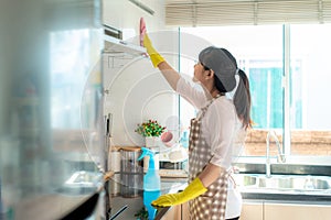 Asian woman wearing rubber protective gloves cleaning kitchen cupboards in her home during Staying at home using free time about