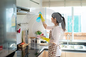 Asian woman wearing rubber protective gloves cleaning kitchen cupboards in her home during Staying at home using free time about