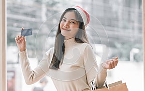 Asian woman wearing santa hat, holding credit card and shopping bag