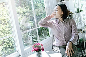 Asian woman wearing a shirt, wearing glasses, sitting in a room, looking out the window