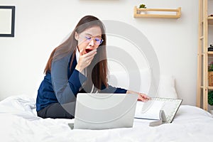 Asian woman wearing a suit bring work to do at home, sit and work on the bed She was drowsy.
