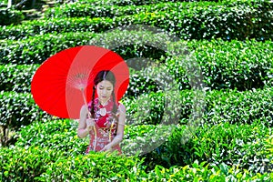 Asian woman wearing traditional Chinese dress and red umbrella in green tea field