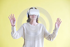 Asian woman wearing virtual reality, VR headset and trying to touch something with hand while stand over isolated yellow