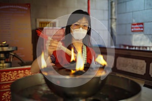 Asian woman wearing a white mask lights incense on an oil burner in a shrine photo