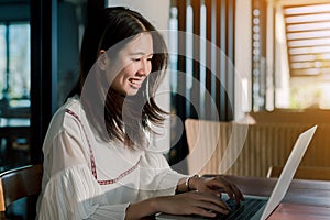 Asian woman Wearing a white shirt sitting in front of a laptop computer With a happy smile