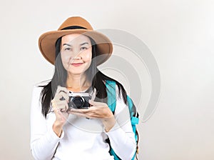 Asian woman wearing  white t-shirt and hat , holding camera and carrying backpack, smiling and looking at camera. Travelling