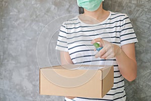 Asian woman wears mask using spray alcohol sanitizer cleaning parcel post, to prevent the virus and bacterias from postal sender,