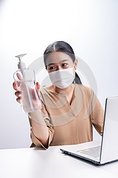 Asian woman wears protective mask presenting alcohol gel on white background