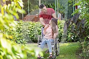 Asian woman on wheelchair and smiling with her husband. A Man standing behind wheelchair and is encouraging his wife, whose feet h