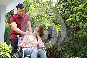 Asian woman on wheelchair and Unhappy and painful. A Man standing behind wheelchair and is encouraging his wife, whose feet hurt h