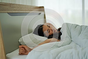 Asian woman on white pillow and bed sheet in bedroom relaxing on holiday stay home