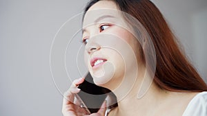 Asian woman in white room near window, talking on the phone with normal feeling. neither happy nor sad.