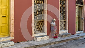 Asian woman in white t-shirt  in Athens in white hat and sarong leaning against wall with large windows photo