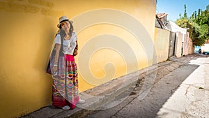 Asian woman in white t-shirt  in Athens in white hat and sarong leaning on yellow wall photo