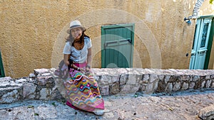 Asian woman in white t-shirt  in Athens in white hat and sarong sitting on stone wall photo