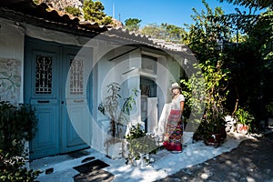 Asian woman in white t-shirt in Athens in white hat and sarong standing in front of house photo