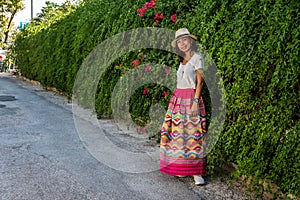 Asian woman in white t-shirt in Athens in white hat and sarong standing in front of ivy wall with flowers photo