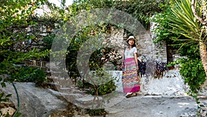 Asian woman in white t-shirt in Athens in white hat and sarong standing in garden in front of wall photo