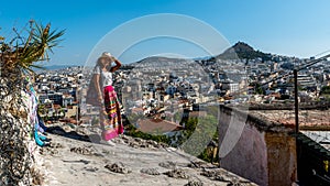 Asian woman in white t-shirt in Athens in white hat and sarong standing on hill above Athens holding her hat photo