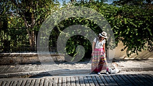 Asian woman in white t-shirt in Athens in white hat and sarong looking down at cat photo