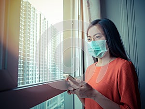 Asian woman, who is wearing a mask, is holding her mobile phone