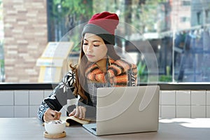 Asian woman in winter-wears with laptop offsite work casually in the coffee shop