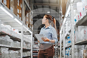 Asian woman worker working with digital tablet checking boxes Logistic import and export supplies packages in Warehouse ,