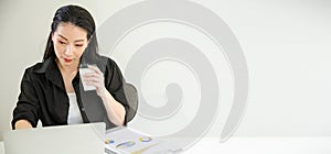 Asian woman working at desk in a creative office and holding a cup of coffee with annual report paper on table. Work from home