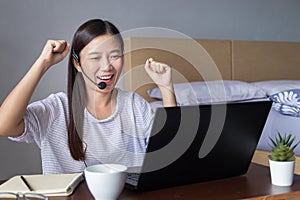 Asian woman working at home with headset making video conference with colleagues via laptop computer , feeling happy excited