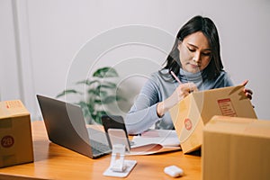 Asian woman working laptop computer from home on the table with postal parcel, Ecommerce business, Selling online concept