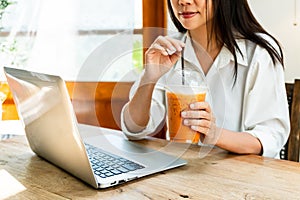 Asian woman working on laptop while drinking milk tea in coffee shop. Technology and lifestyle, work from anywhere concept