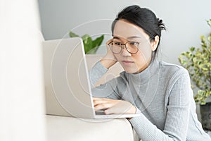 Asian woman is working  a laptop in the living room. She sit on the floor and sofa is office desk