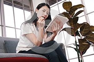 Asian woman is working and writing on notebook. She is thinking and serious for business in sofa at office. Lifestyle of