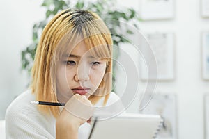 Asian woman write shopping lists in notepad by pen on her kitchen counter at home.