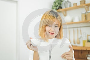 Asian woman write shopping lists in notepad by pen on her kitchen counter at home.