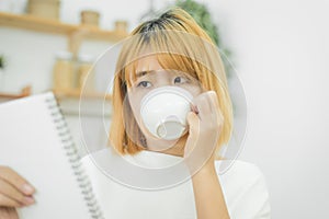 Asian woman write shopping lists in notepad by pen on her kitchen counter at home.