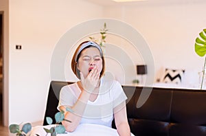 Asian woman yawning covering open mouth with hand sitting on sofa, Tired sleepy,Female with symptoms sleepiness