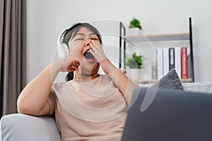 Asian woman is yawning while studying, working, or watching a movie on the sofa in the living room at home