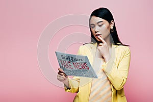 Asian woman in yellow outfit reading newspaper with fake news  on pink