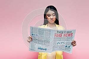 Asian woman in yellow outfit reading newspaper with fake news  on pink