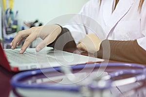 Asian womanâ€™s hand doctor typing keyboard of laptop for working and blurred stethoscope on the desk at the hospital office