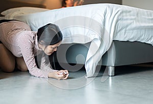 Asian women bent and searching something under bed lost thing in bedroom