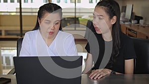 Asian women co-workers in workplace including person with blindness disability using laptop computer with screen reader program