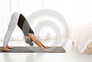 Asian women doing yoga exercise at home, stretching in Downward Facing Dog pose or adho mukha svanasana in white bedroom.  Working