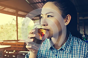 Asian women drink soft drink soda in sunny day at restaurant, glass of cola with ice in women hand