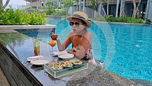 Asian women drinking cocktails by the bar of a tropical pool during vacation