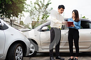 Asian women driver Talk to Insurance Agent for examining damaged car and customer checking on report claim form after an accident