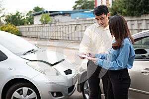 Asian women driver Talk to Insurance Agent for examining damaged car and customer checking on report claim form after an accident