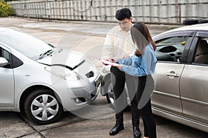 Asian women driver Talk to Insurance Agent for examining damaged car and customer checking on report claim form after an accident